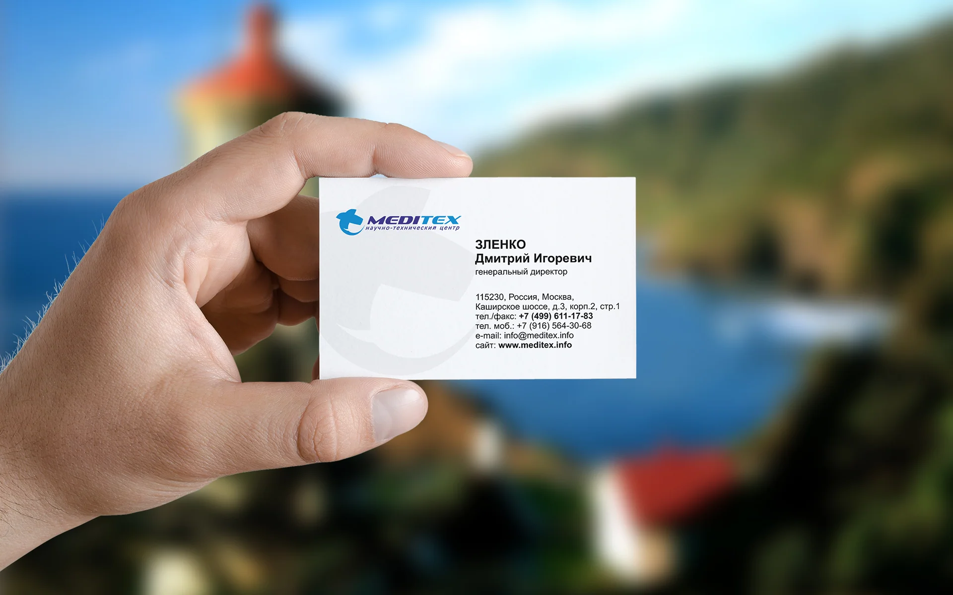 Белая визитка Meditex в руке на фоне побережья