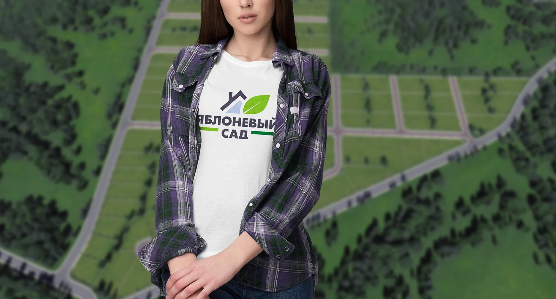Девушка в футболке с логотипом «Яблоневый сад» на фоне генплана участков