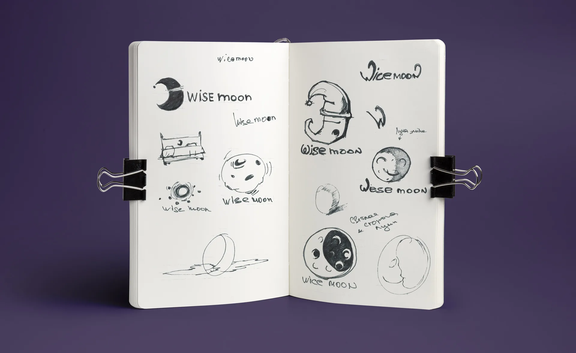 Эскизы логотипа Wisemoon в раскрытом блокноте на фиолетовом фоне